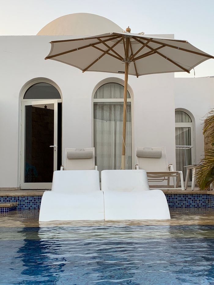 Luxurious poolside view with modern architecture, sun loungers, and parasol. Tranquil escape in a serene setting.